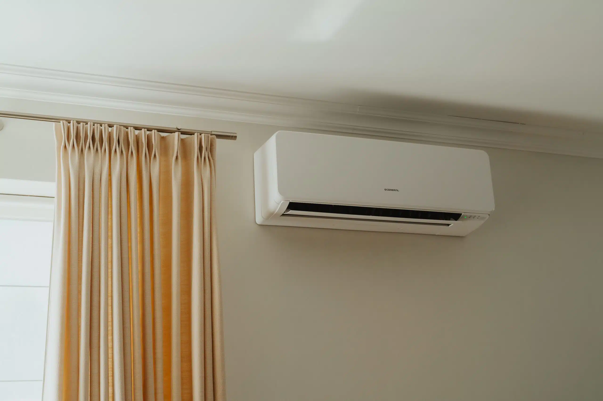 Witte split airco unit geïnstalleerd aan muur naast goudkleurige gordijnen voor huishoudelijke klimaatbeheersing