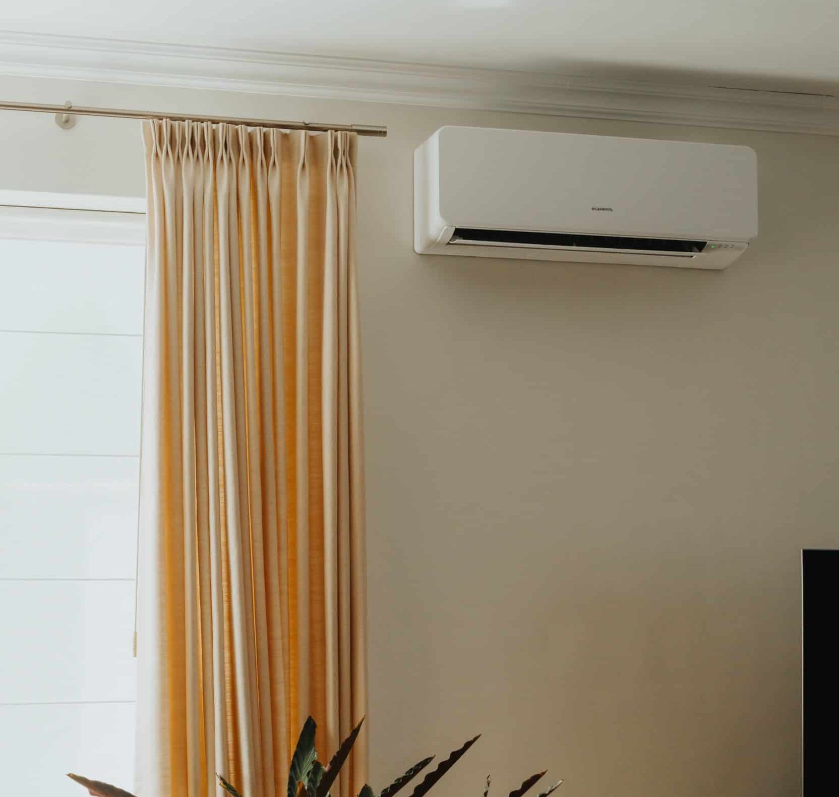 Moderne witte airco unit geïnstalleerd aan muur met beige gordijnen in woonkamer