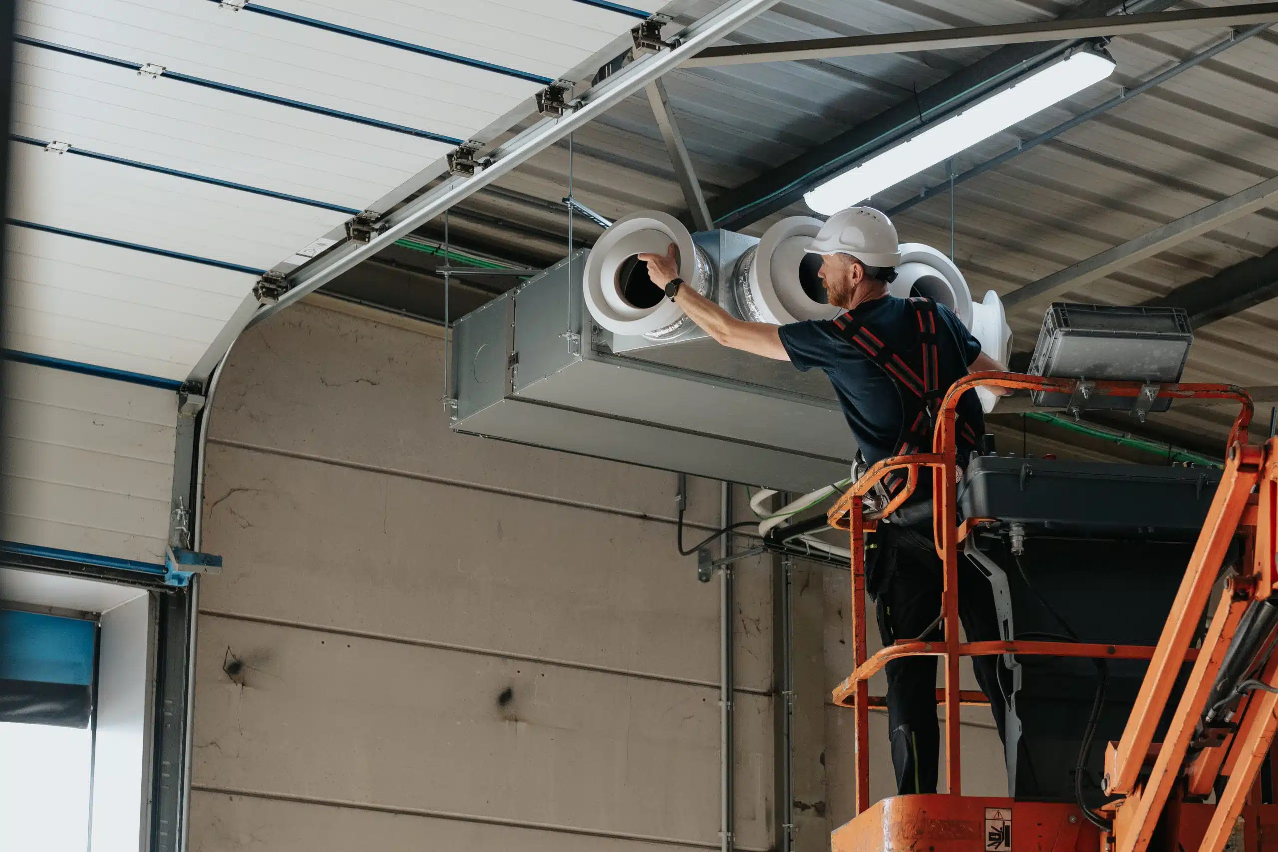 Technicus installeert ventilatie-eenheid op bedrijfslocatie met hoogwerker voor doelmatige luchtcirculatie